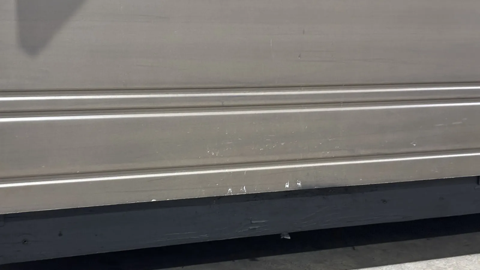 Close-up of a metal rolling shutter door showing horizontal lines and scratches at the bottom section.