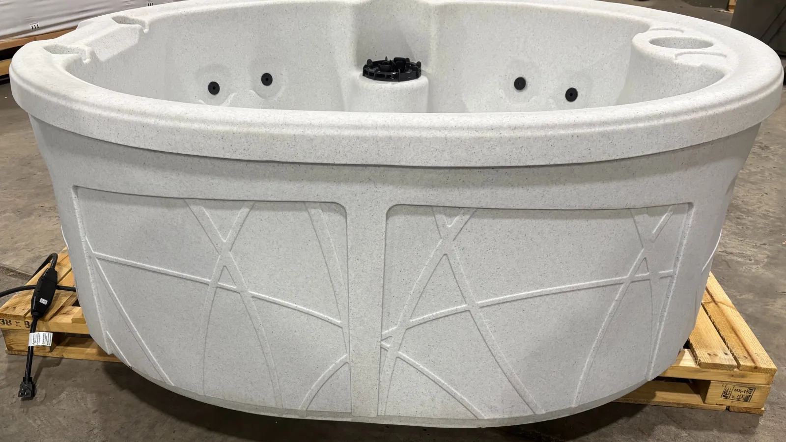 White round hot tub with jets and textured exterior on wooden pallet in warehouse setting