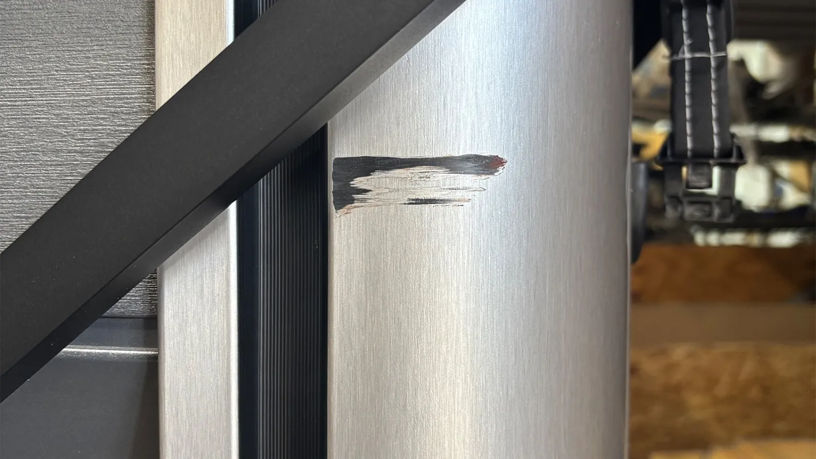 Close-up of a scratched metallic surface with black scuff marks next to a black diagonal bar.