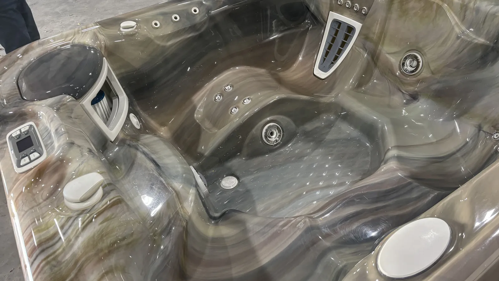 Modern fiberglass hot tub interior with multiple seats, jets, and control panels in gray and brown tones