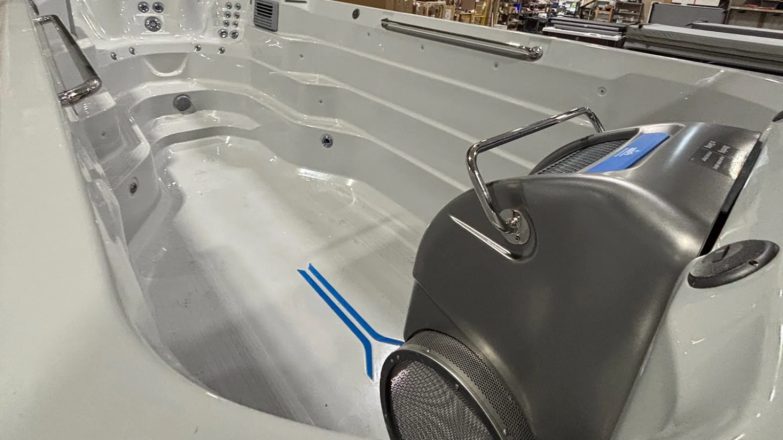 Empty modern swim spa with stainless steel handrails and built-in water jets in a warehouse setting