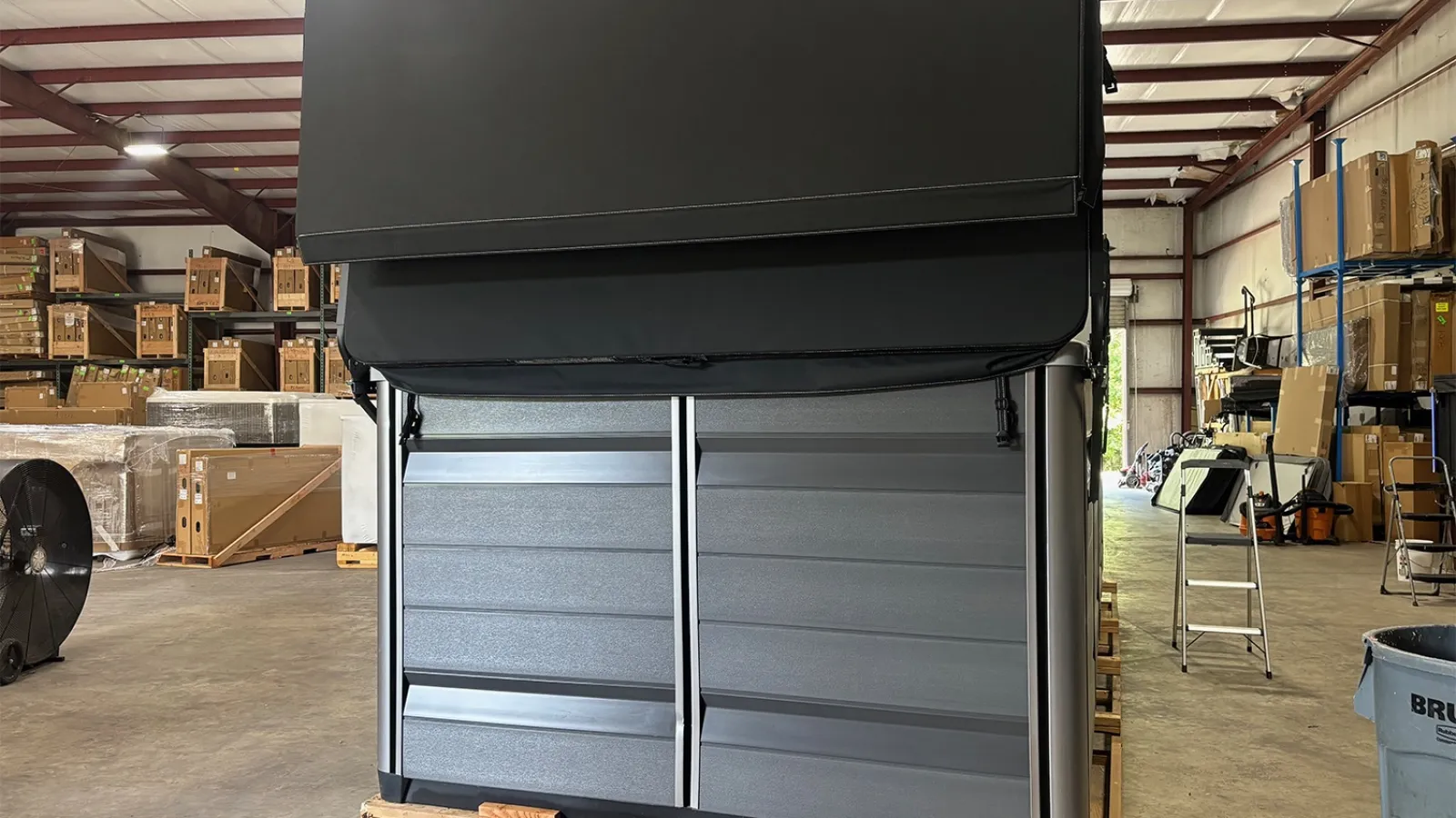 Warehouse interior with stacked cardboard boxes and a large black and gray industrial equipment on a pallet.