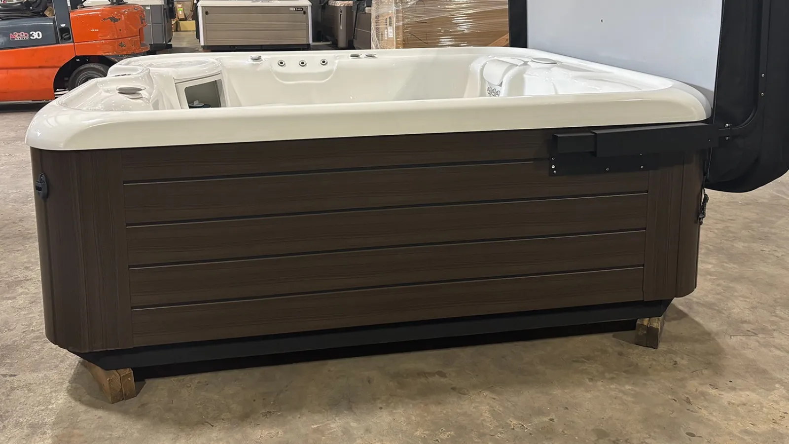 Modern rectangular hot tub with white interior and brown wood-textured exterior in warehouse setting