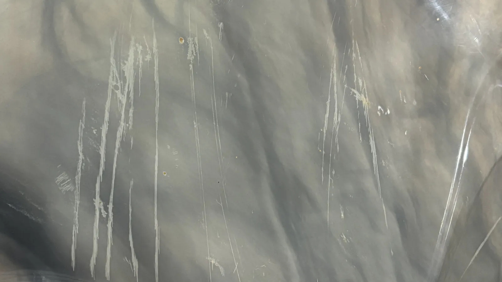 Close-up of gray scratched metal surface with vertical and diagonal scuff marks and small dents.