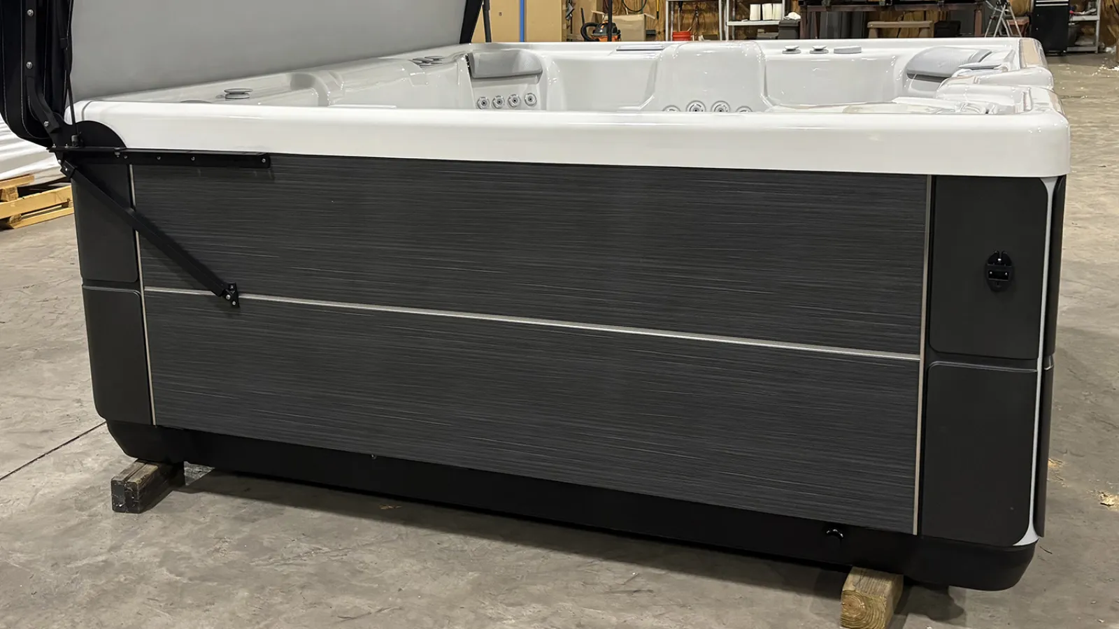 Modern gray and white hot tub with multiple jets in a warehouse setting on wooden blocks
