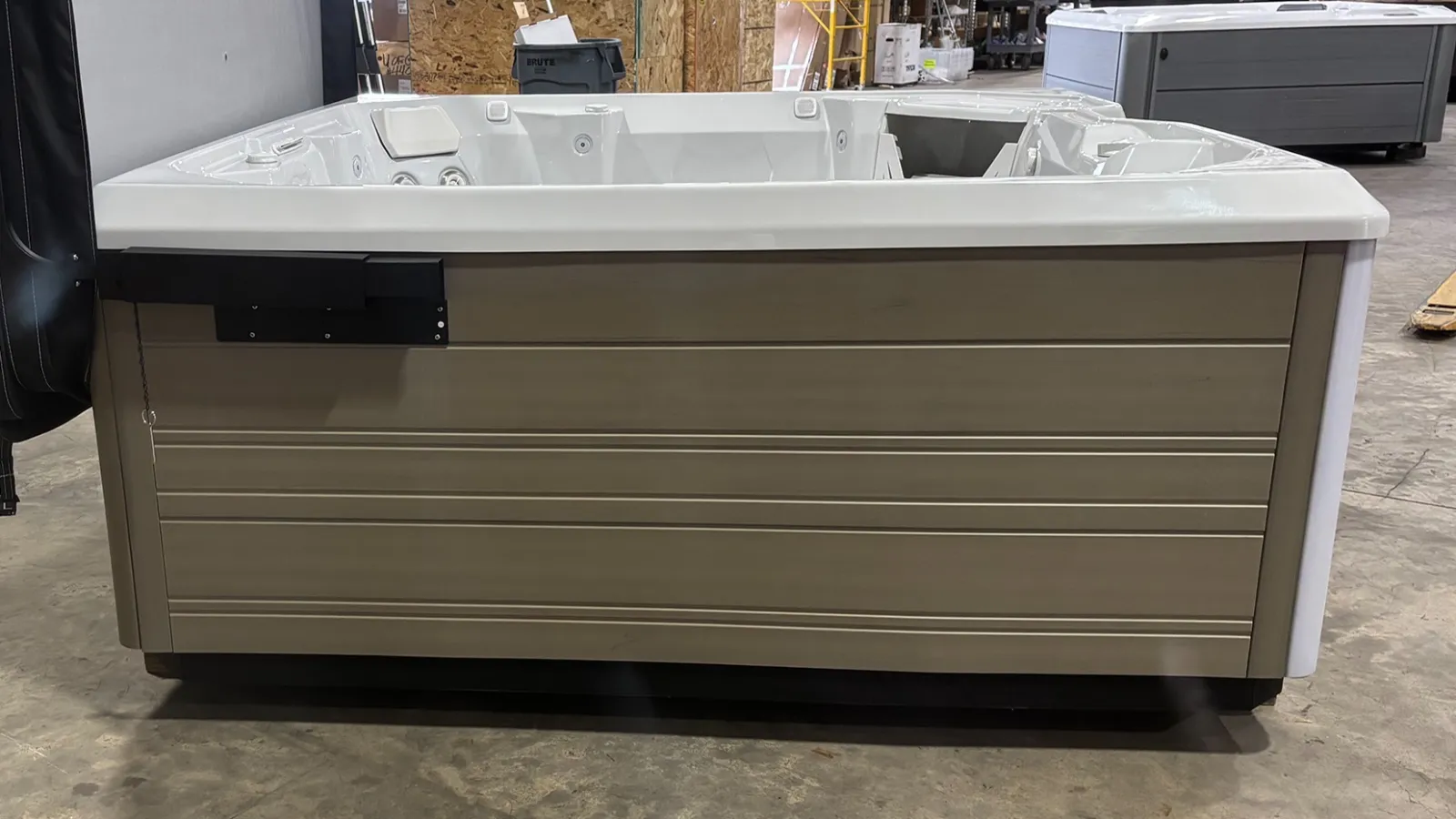 Large white indoor hot tub with beige exterior panels on concrete floor in warehouse setting