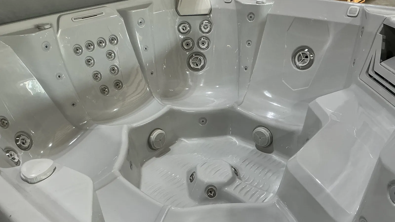 Interior of an empty white hot tub with multiple jet nozzles and contoured seating for several people.