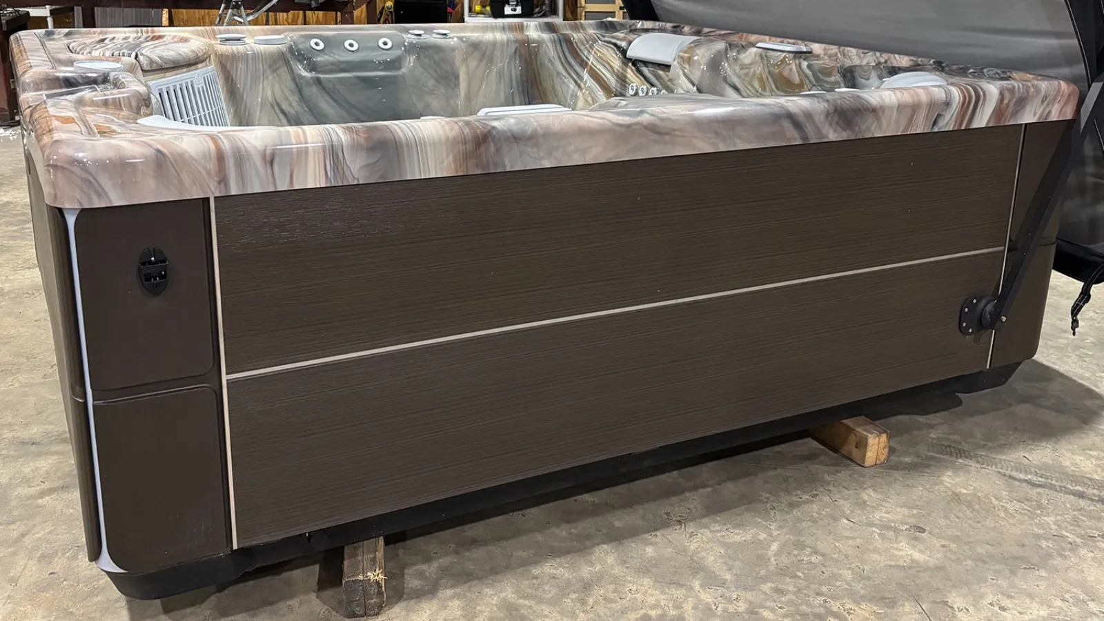 Large brown and marble-patterned hot tub with jets, placed indoors on concrete floor with protective supports.