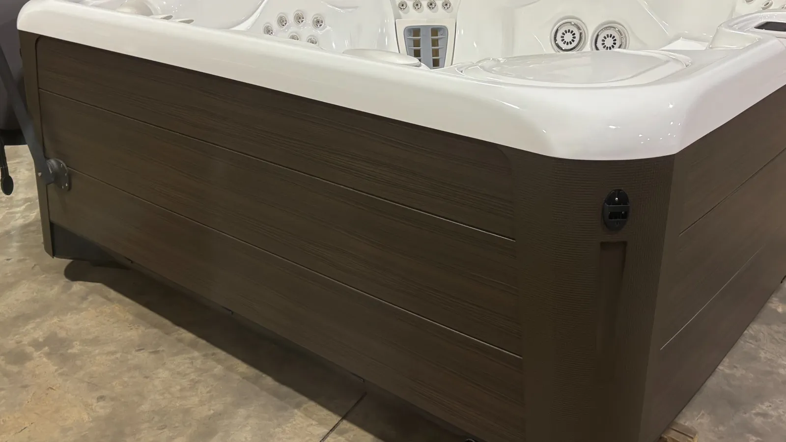 Corner view of a modern hot tub with white interior and brown wood-look exterior panels on concrete floor.