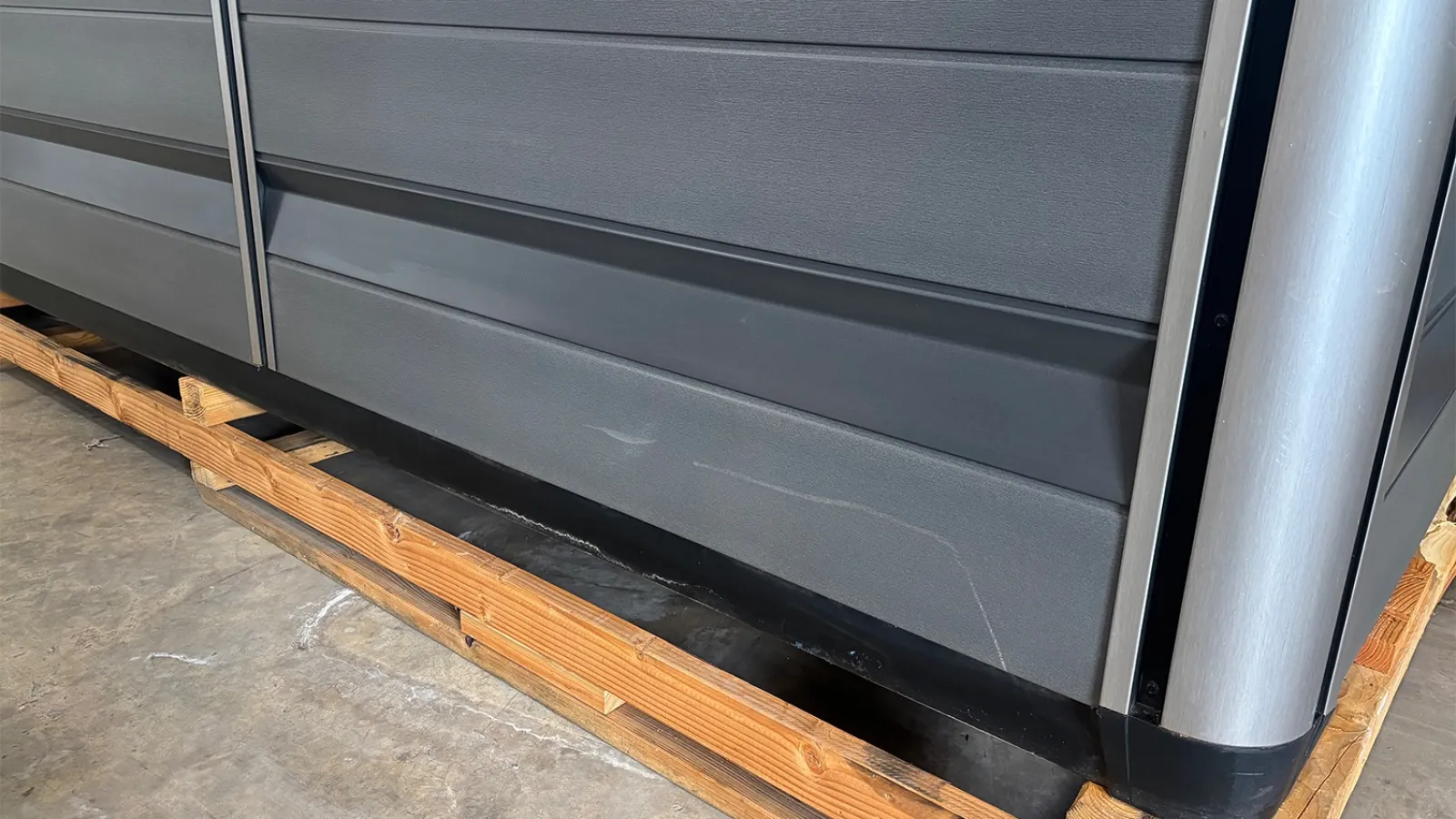 Black and gray metal cabinet or storage unit sitting on wooden pallets on a concrete floor.