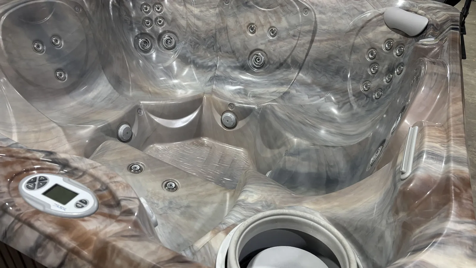 Modern gray marble-patterned hot tub with multiple jets, a digital control panel, and headrest for relaxation.