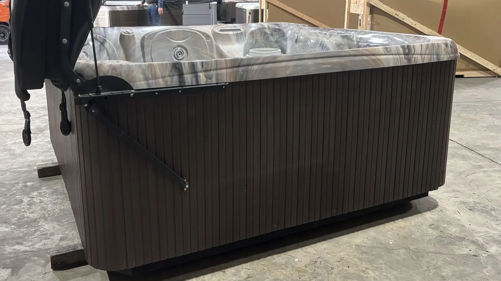 Modern rectangular hot tub with marbled interior and dark wooden exterior in a showroom setting.