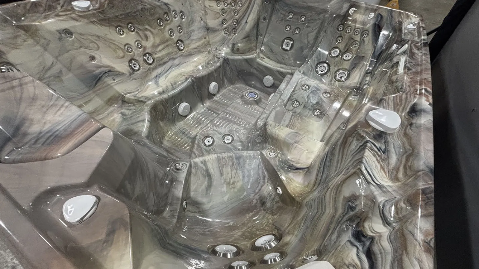 Marbled gray and beige spa hot tub with multiple seating areas and numerous water jets inside.