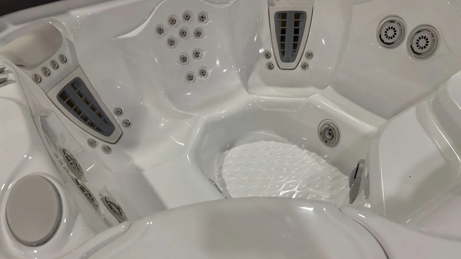 Close-up of a white hot tub interior with multiple water jet nozzles and contoured seating areas.