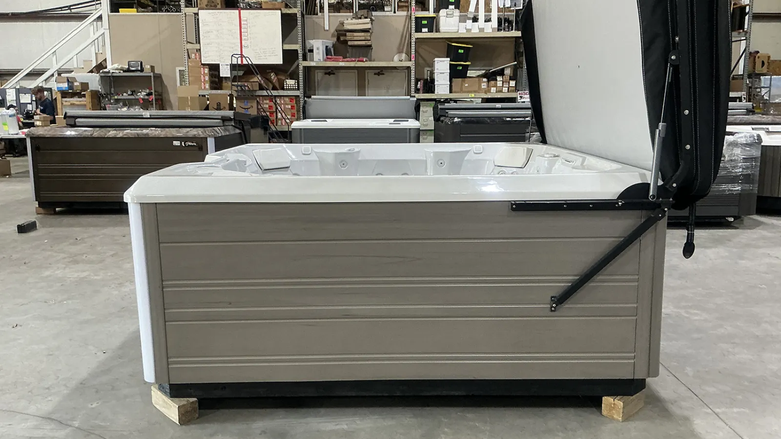 Gray and white hot tub with an open cover inside a spacious warehouse setting.