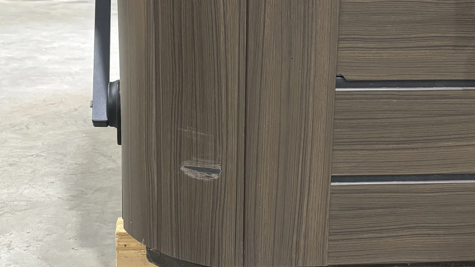 Close-up of a wooden furniture corner with a visible scratch and black base on a concrete floor.