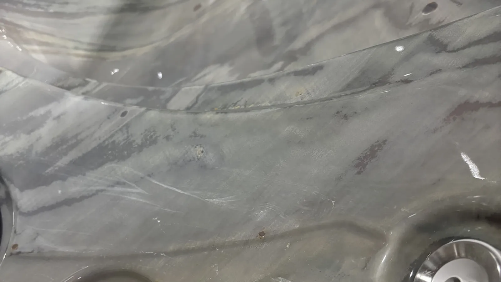 Close-up of a scratched and worn gray metal surface with visible bolts and reflections.