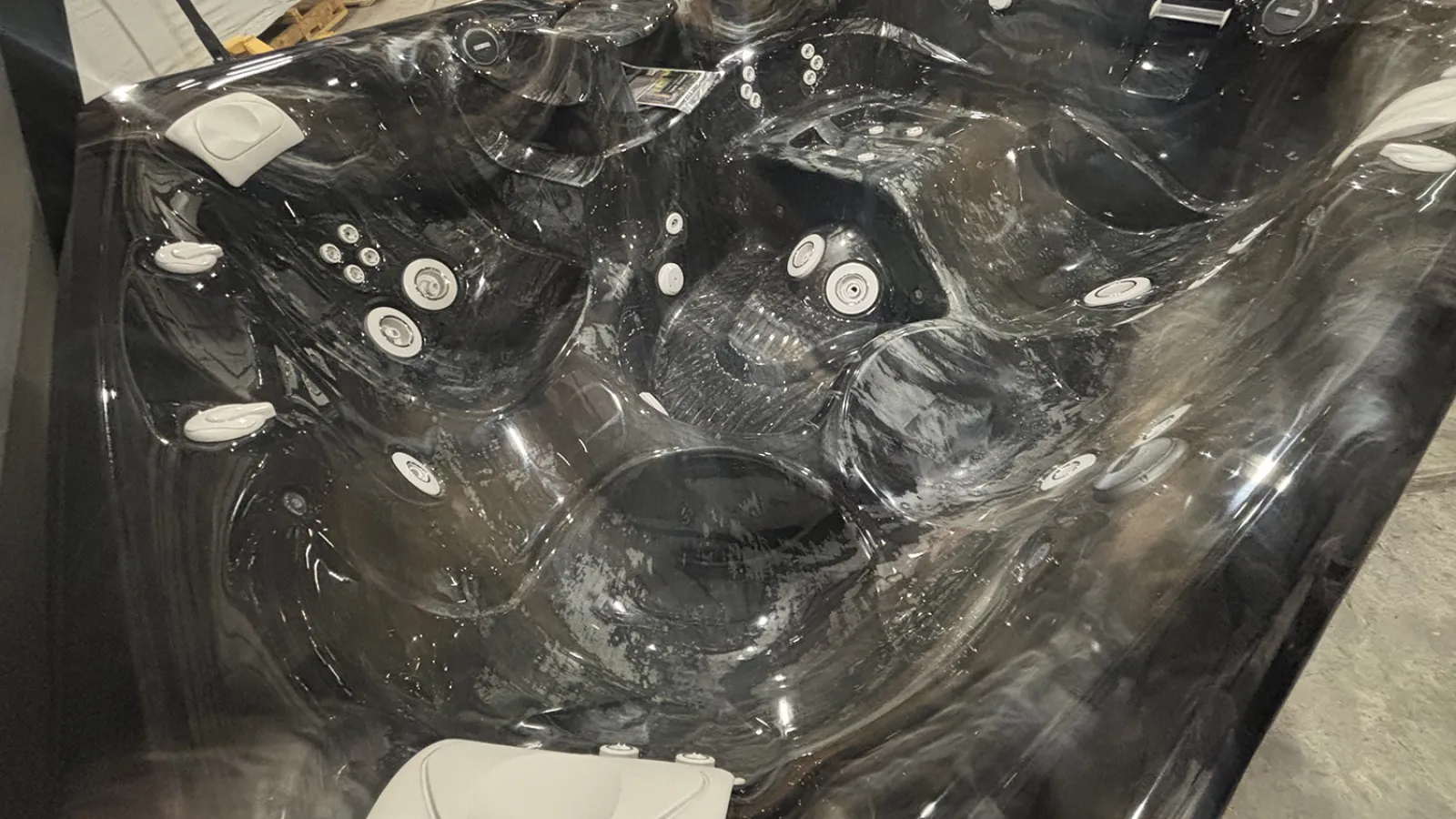 Black marble-patterned hot tub with multiple jets and ergonomic seating in an indoor setting.