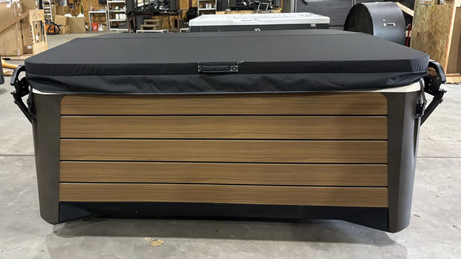 Modern hot tub with wood paneling and black cover in a warehouse setting on concrete floor.