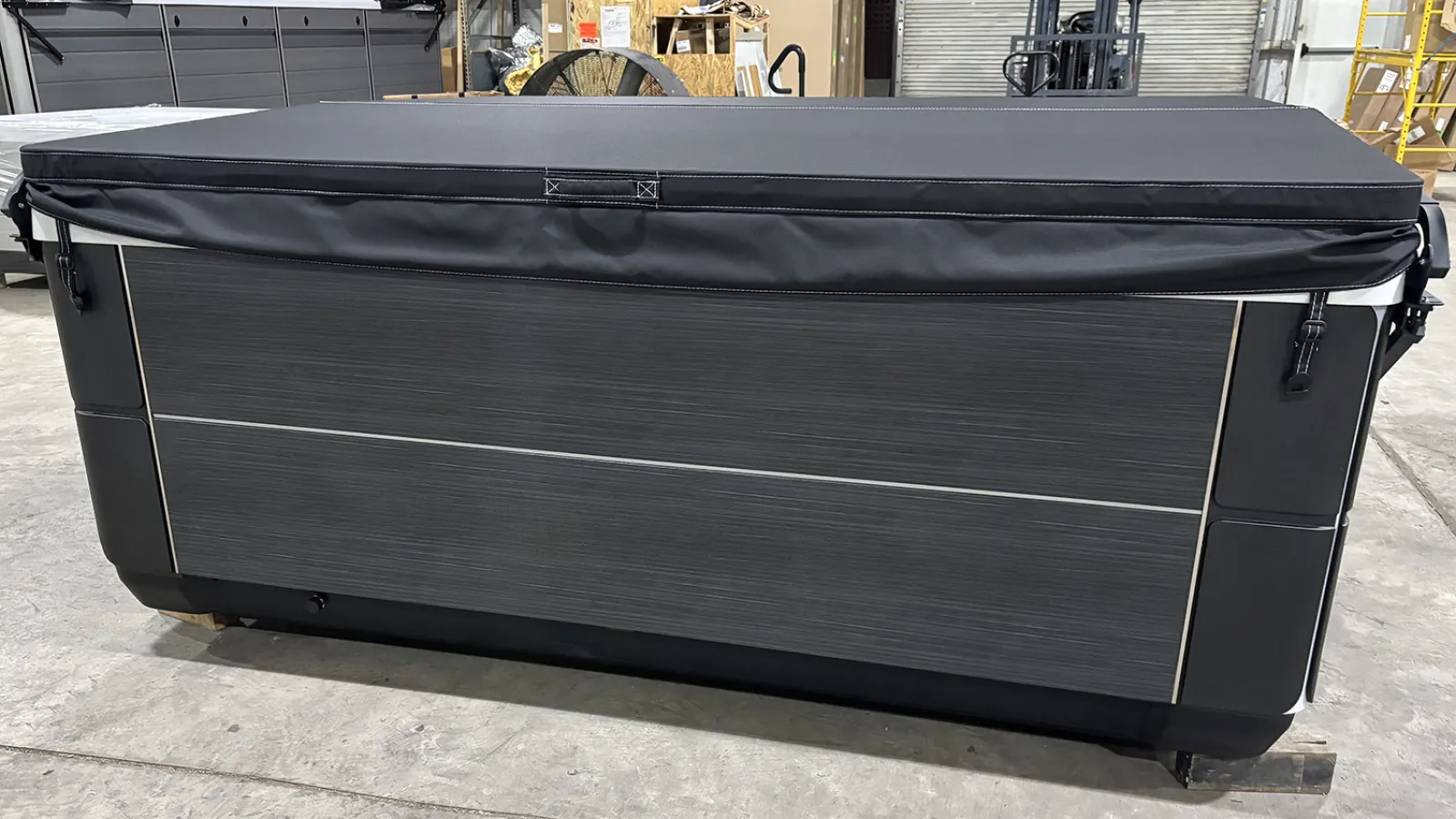 Modern rectangular hot tub with closed black cover in an industrial warehouse setting.