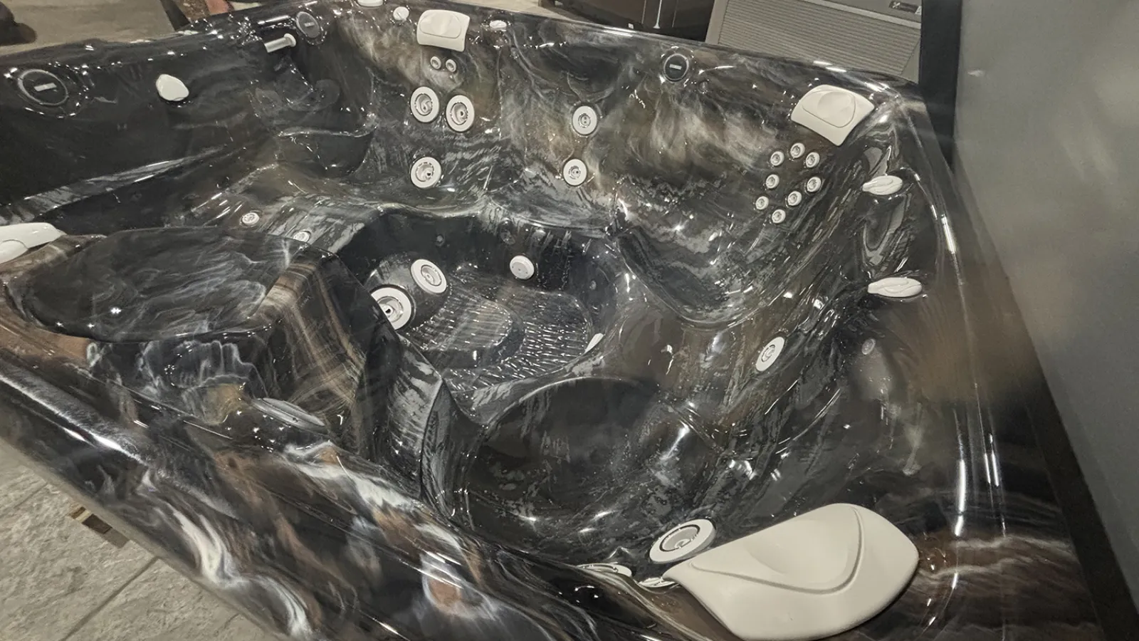 Black and brown marble-patterned hot tub with multiple white jets and headrests in an indoor setting.