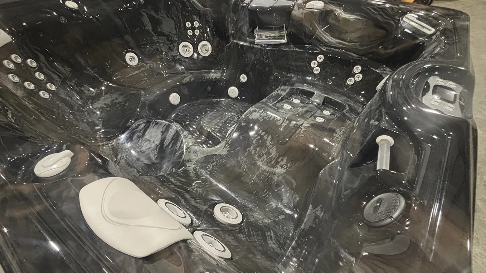 Black glossy hot tub with multiple jets, white control knobs, and built-in headrest in a showroom setting