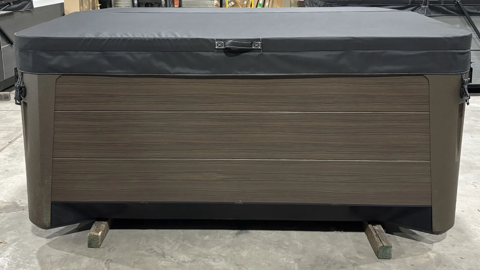 Modern rectangular hot tub with wood-like paneling and a protective black cover in a warehouse.