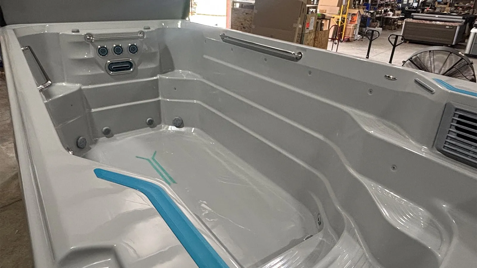 Interior view of a large empty gray and blue spa tub with built-in seats and jets in a warehouse.