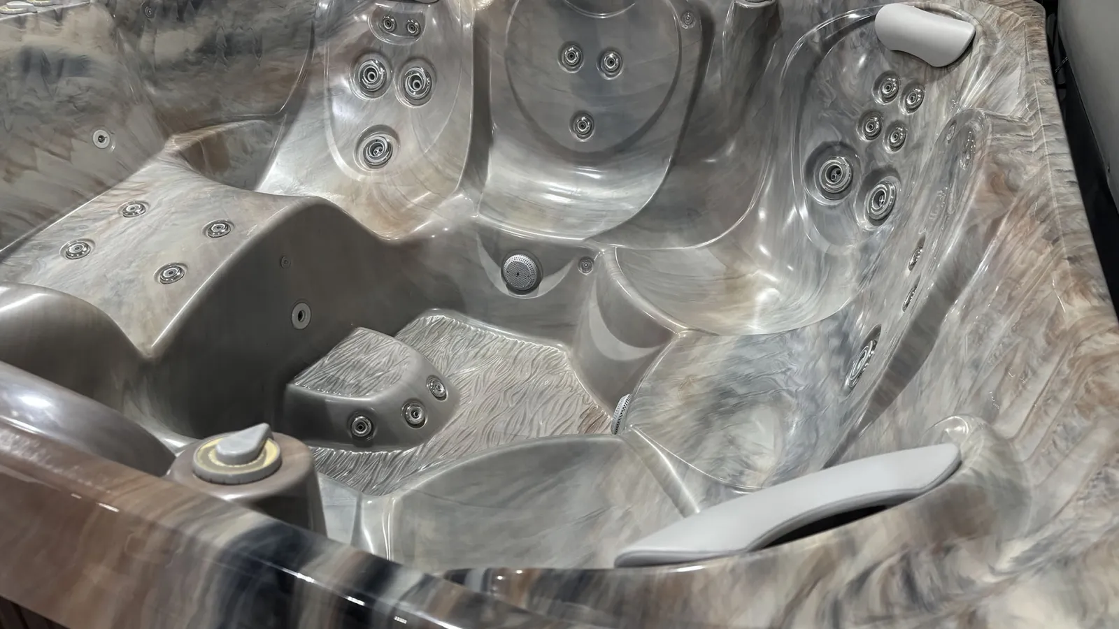 Close-up of a modern gray marble-patterned hot tub with multiple jets and padded headrests.
