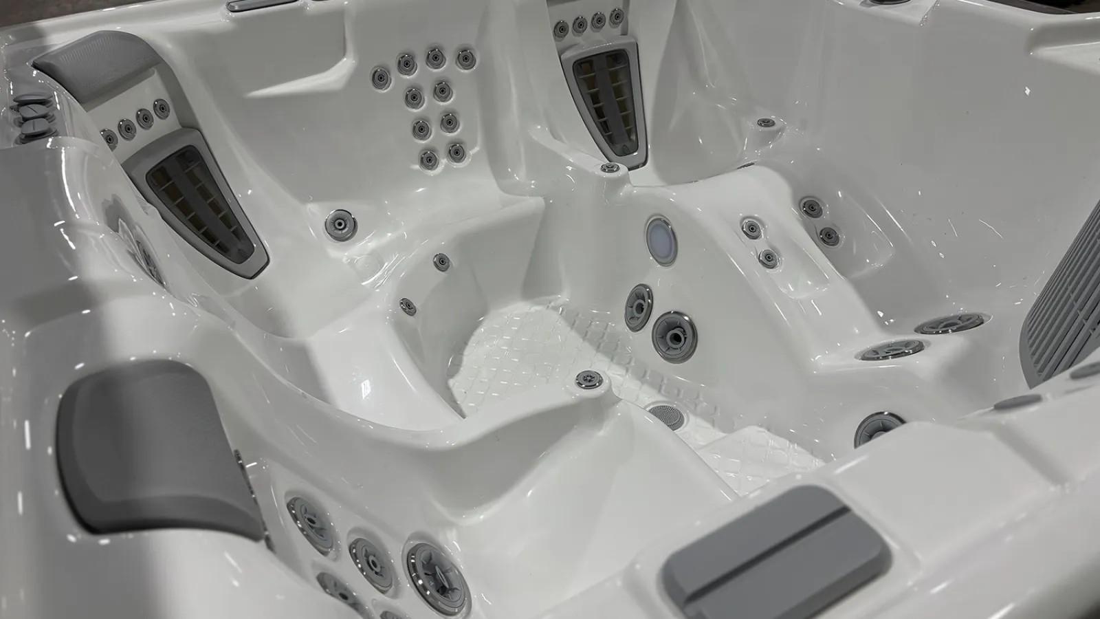 Close-up of an empty white luxury hot tub with multiple water jets and ergonomic seating.