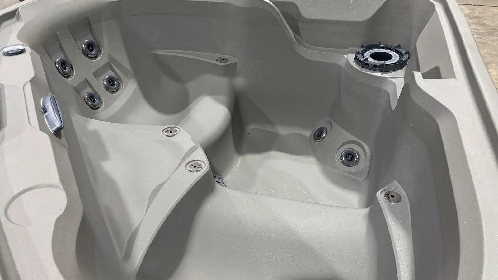 Empty beige outdoor hot tub with multiple jet nozzles and contoured seating in a showroom setting