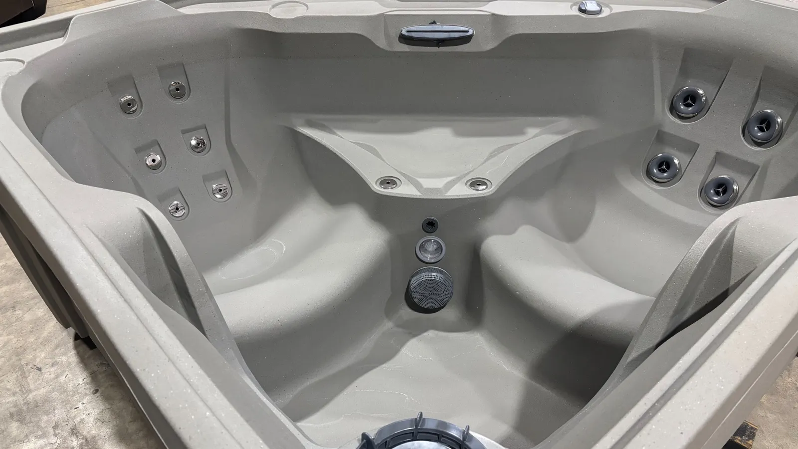 Empty beige hot tub with multiple jet nozzles and built-in seating in an indoor setting.