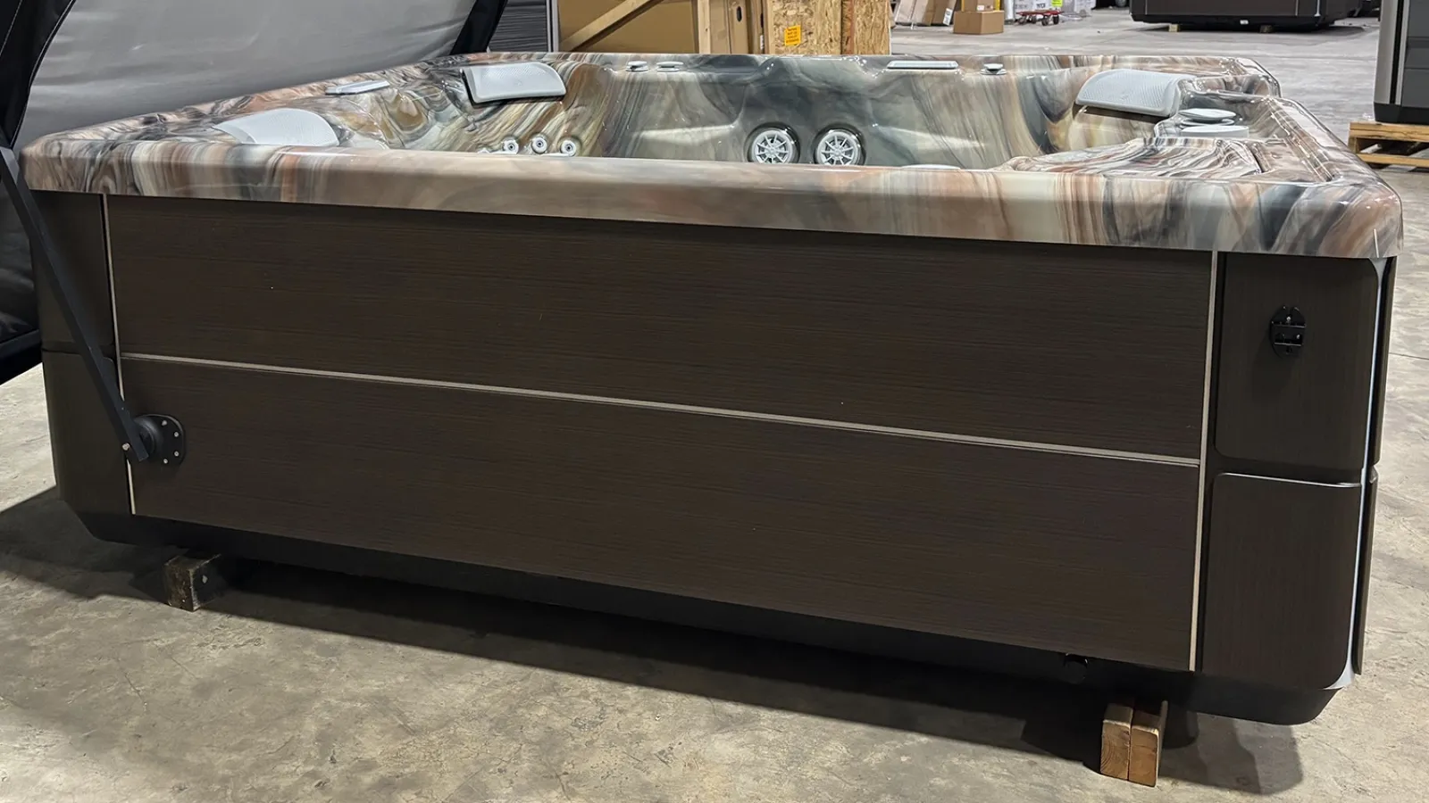 Modern outdoor hot tub with marble-patterned interior and dark wooden exterior panels in warehouse setting