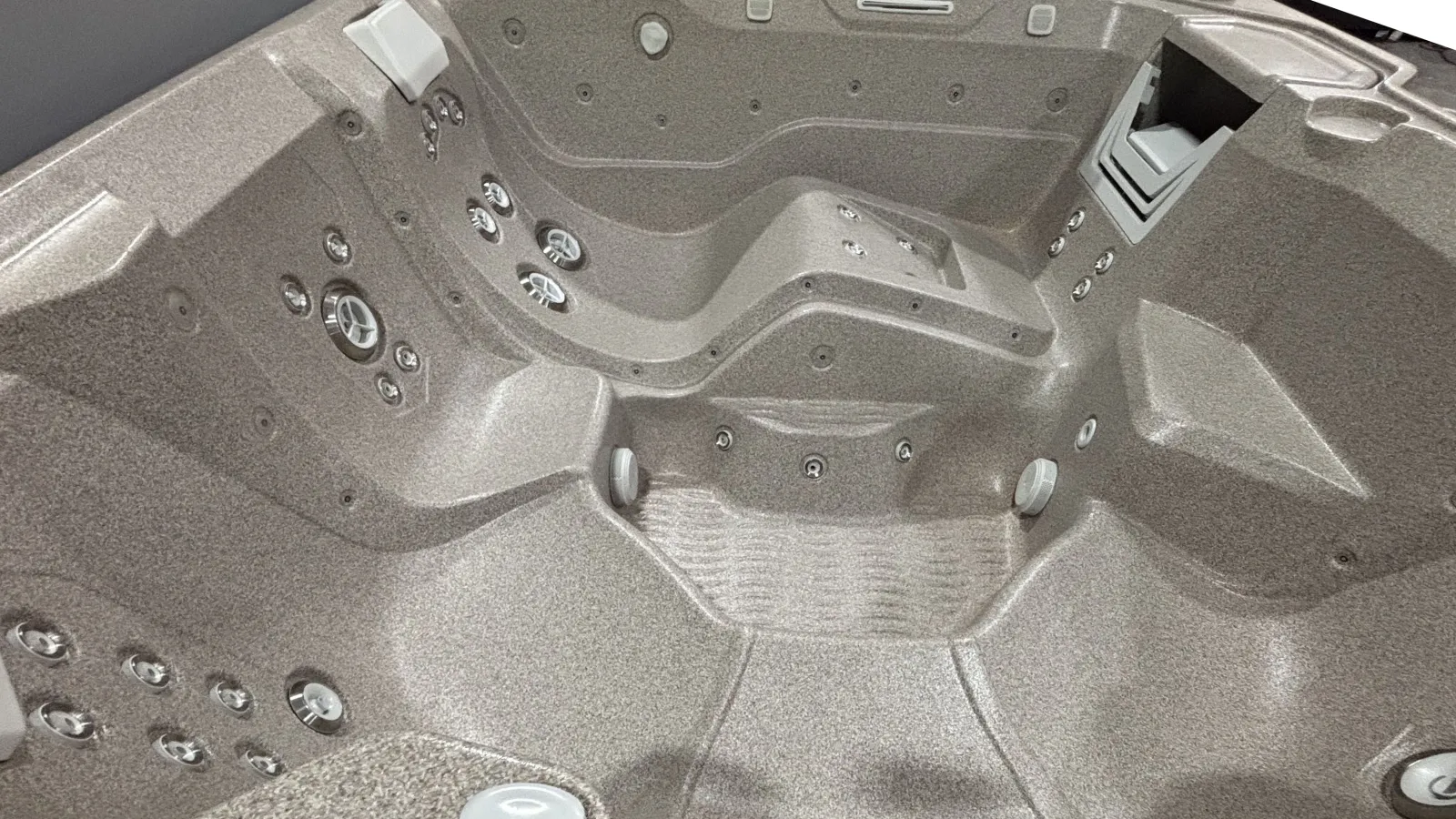 Empty modern hot tub with multiple seating areas and numerous water jets in a textured gray interior.