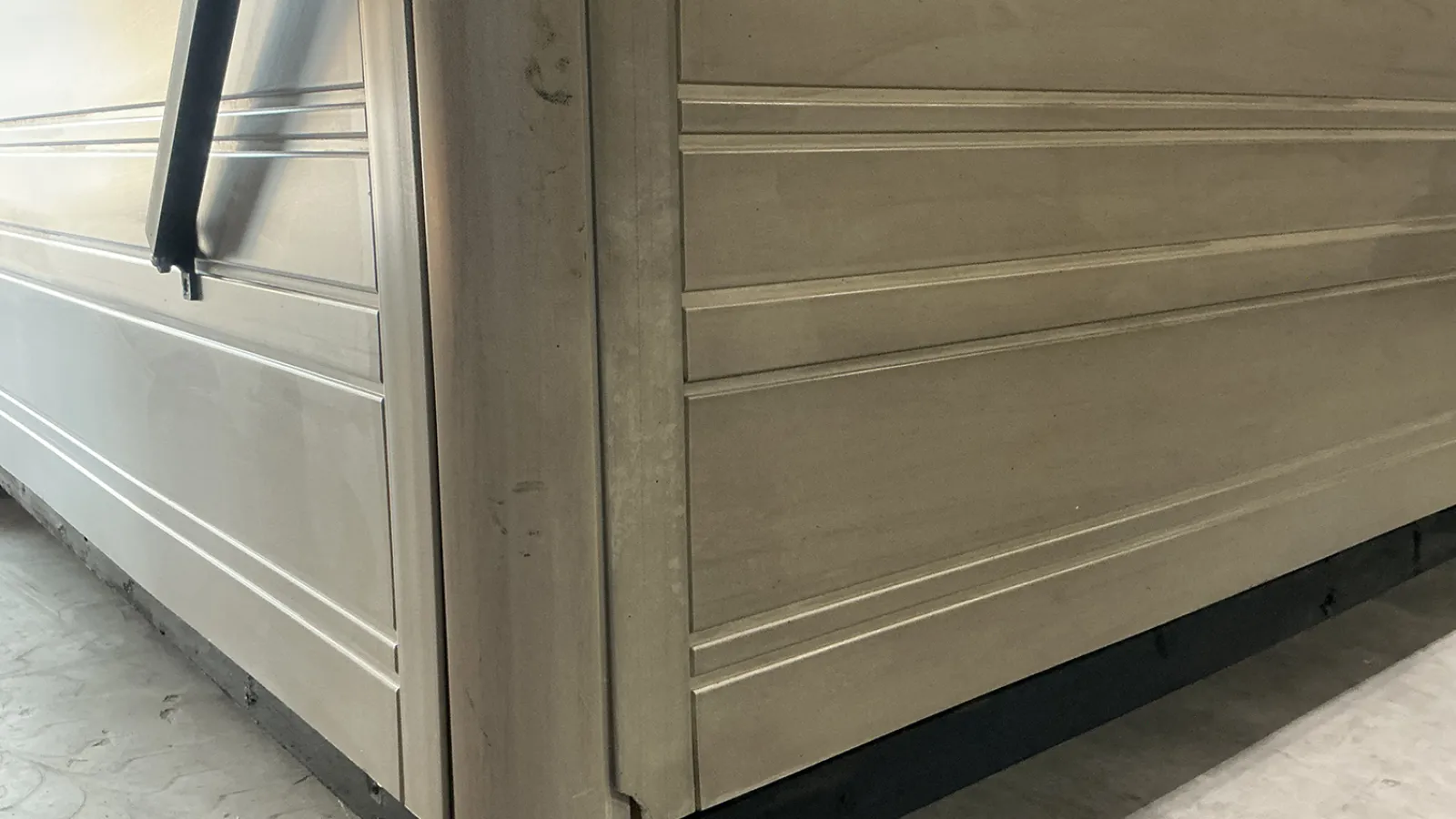 Close-up of a beige sectional garage door with horizontal panels and base trim on concrete floor.