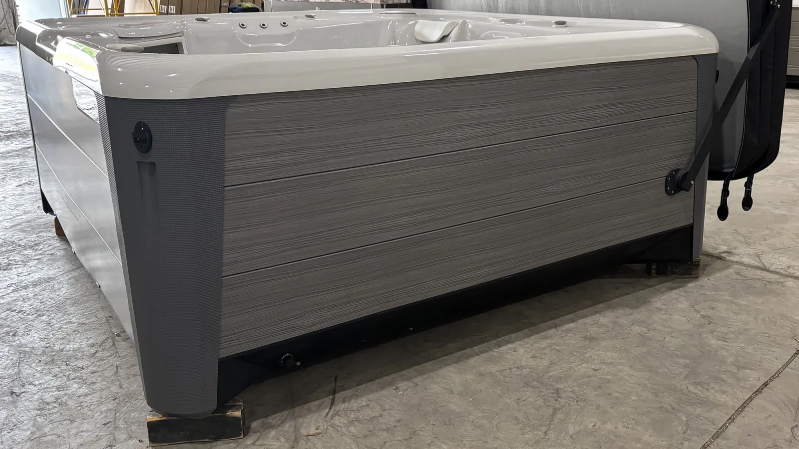 Modern gray and white outdoor hot tub with textured siding placed on concrete floor indoors