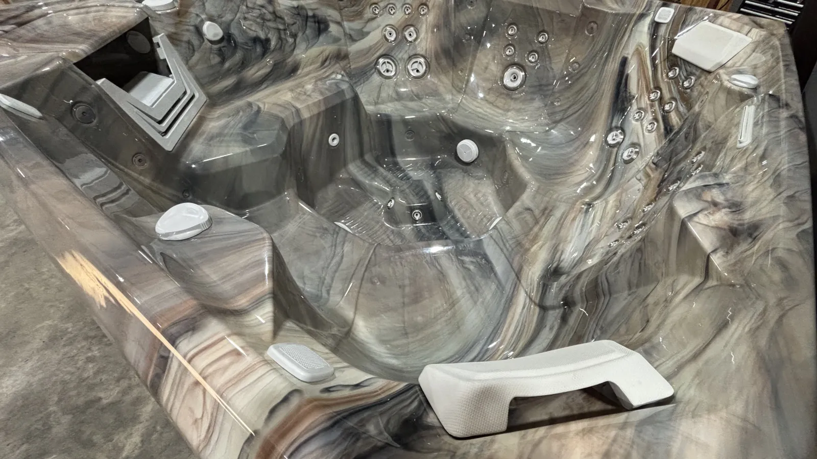 Modern marble-patterned hot tub with multiple jets, ergonomic seats, and white headrests indoors.