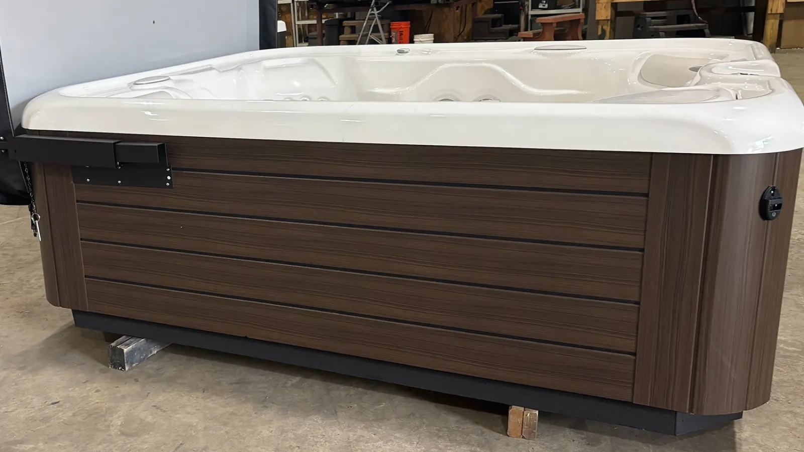 Modern outdoor hot tub with wood-style siding and white interior shell in a warehouse setting.