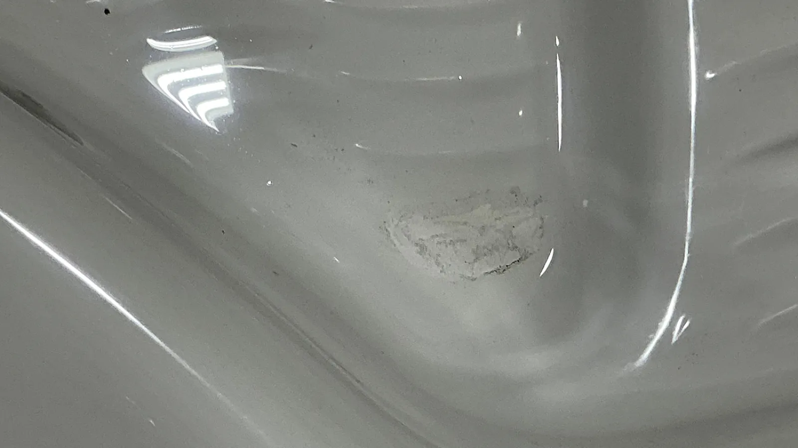 Close-up of a white surface with a smudge or stain and reflective light spots on smooth texture.