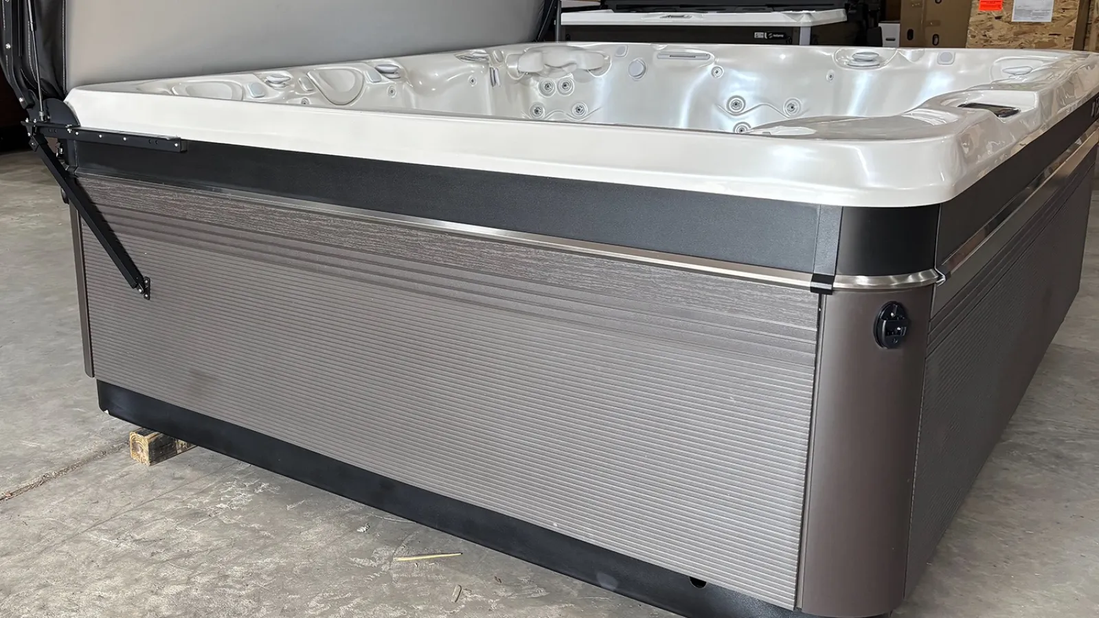 Side view of a gray outdoor hot tub with multiple jets on a concrete floor indoors.