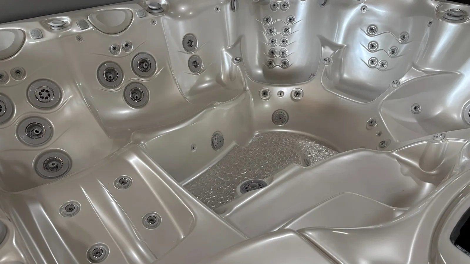 Empty silver hot tub with multiple jet nozzles and ergonomic seating inside a spa pool.
