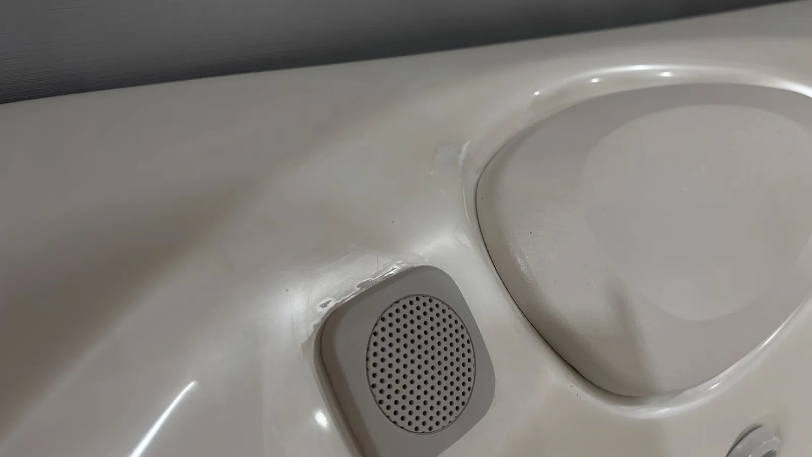 Close-up of a white hot tub or spa interior showing a circular speaker and a rounded corner seat area.
