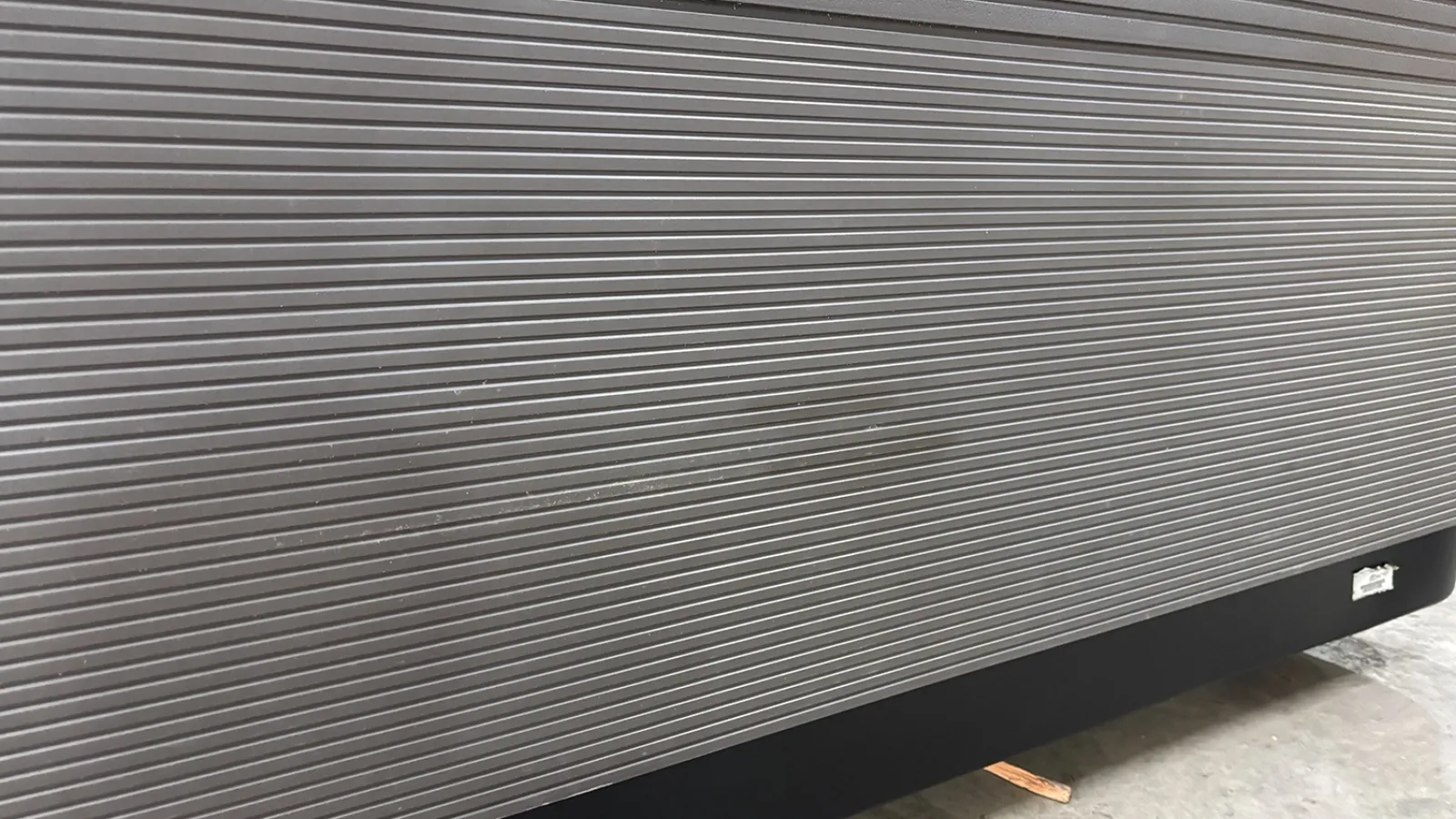 Close-up of a metallic rolling shutter door with horizontal ridges and a concrete floor beneath.
