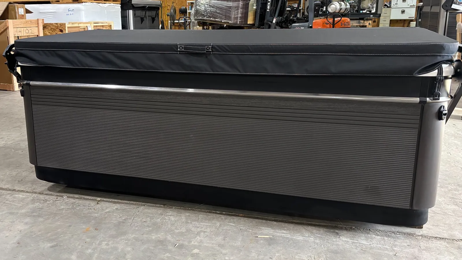 Gray rectangular hot tub with black cover inside a warehouse with wooden crates and equipment.
