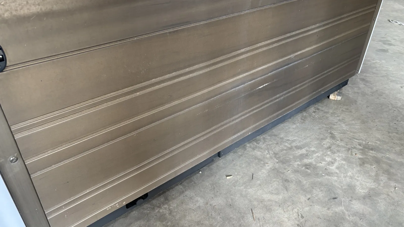 Close-up of a metal garage door with horizontal ridges and a concrete floor beneath it.