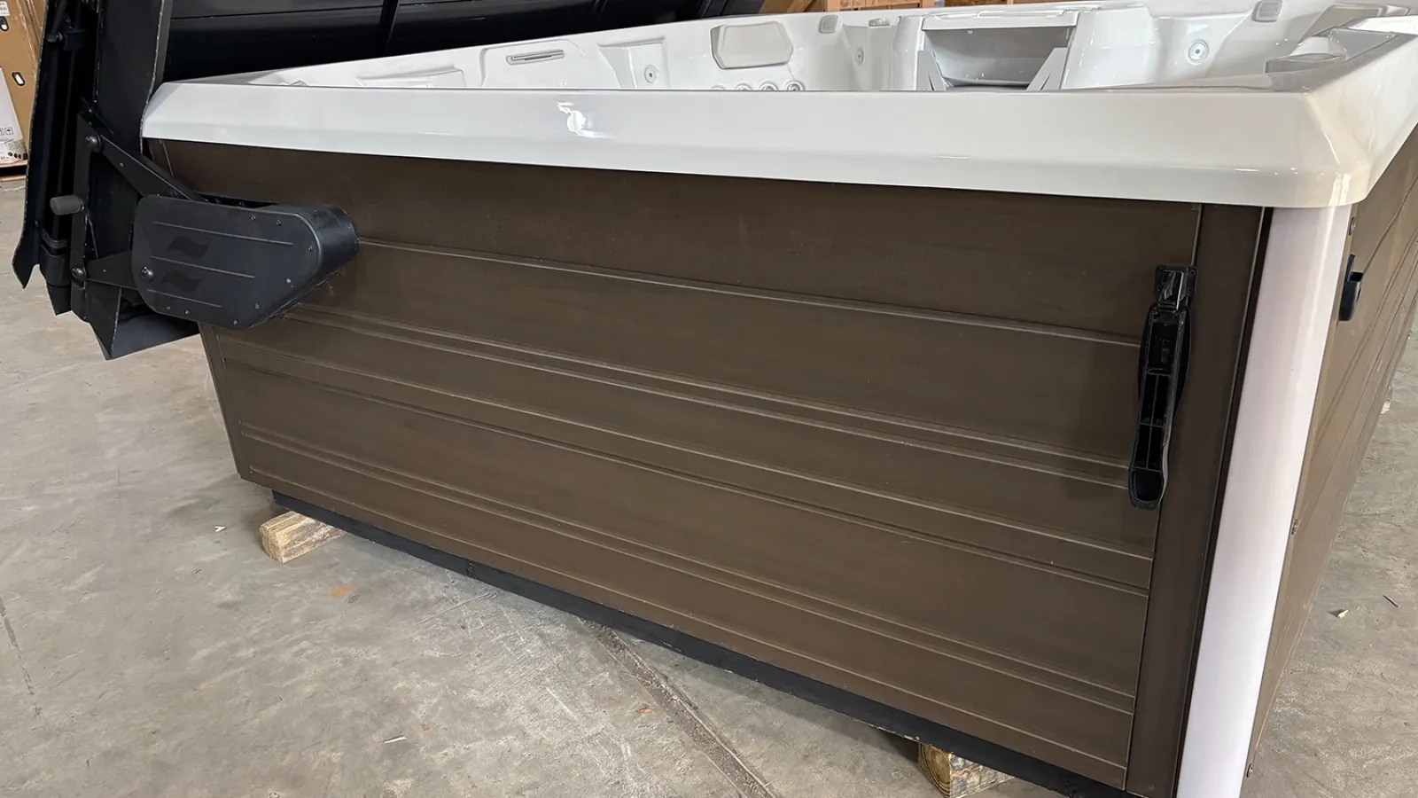 Side view of a large brown and white spa hot tub with cover lifter on a concrete floor.