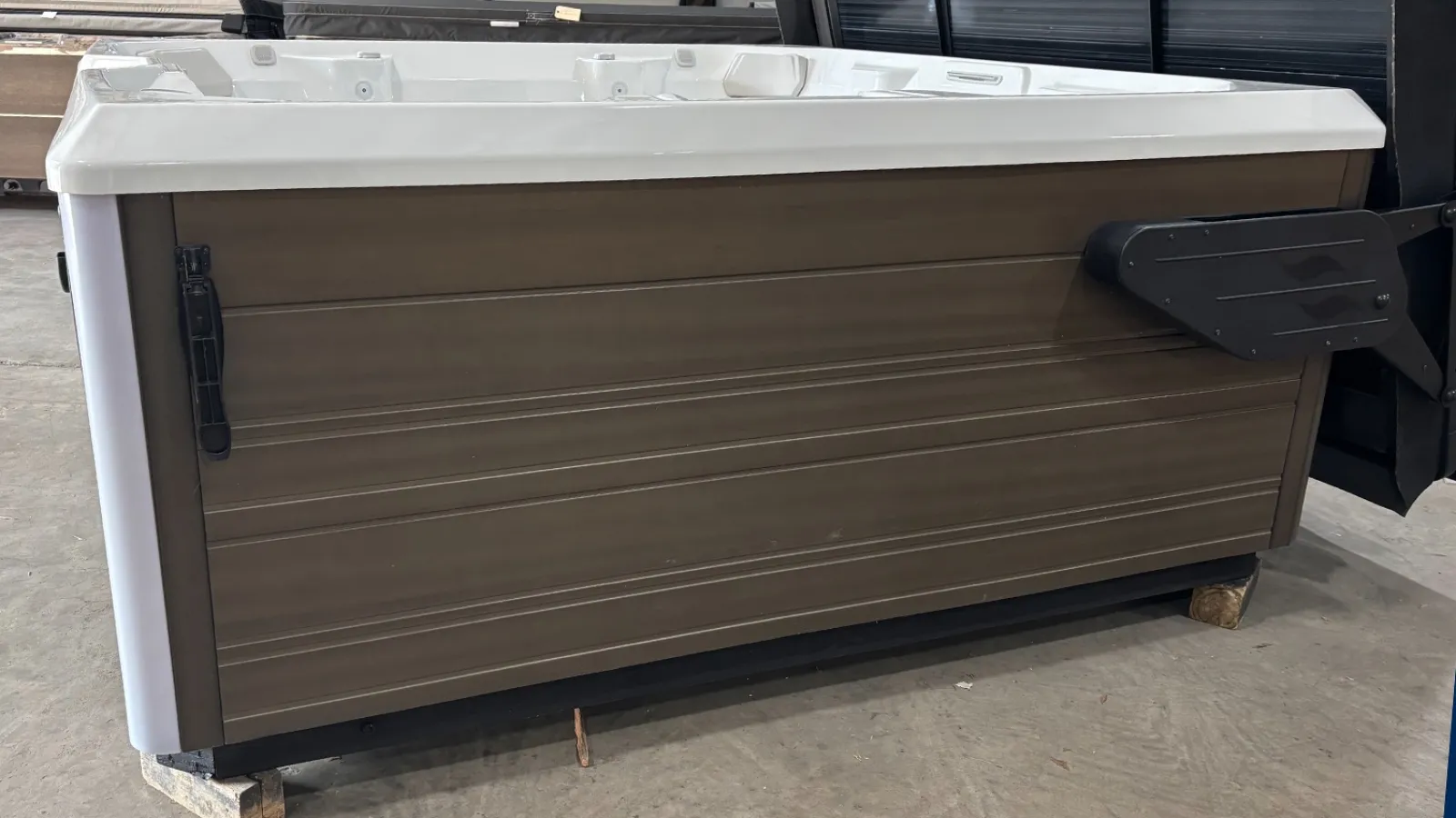 Outdoor hot tub with brown paneling and white top resting on wooden blocks indoors