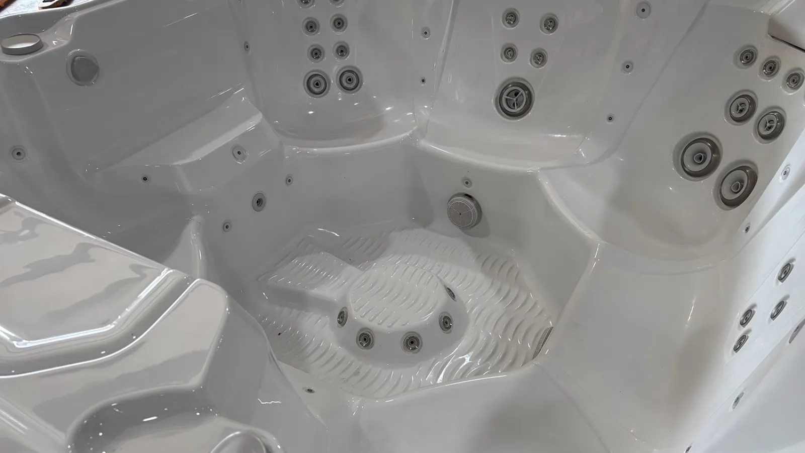 Empty white multi-seat jacuzzi hot tub with multiple water jets and molded seats for hydrotherapy.