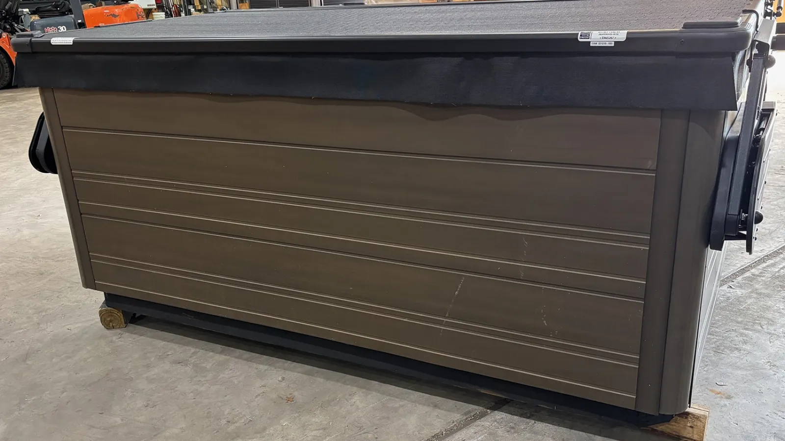 Large brown commercial dumpster with a black plastic lid in indoor warehouse setting.