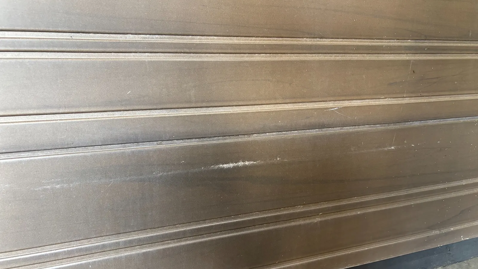 Brown metal rolling garage door with horizontal ridges and visible scratches on the surface.